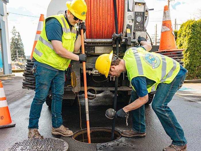 two workers standing behind a truck inspecting a sewer drain