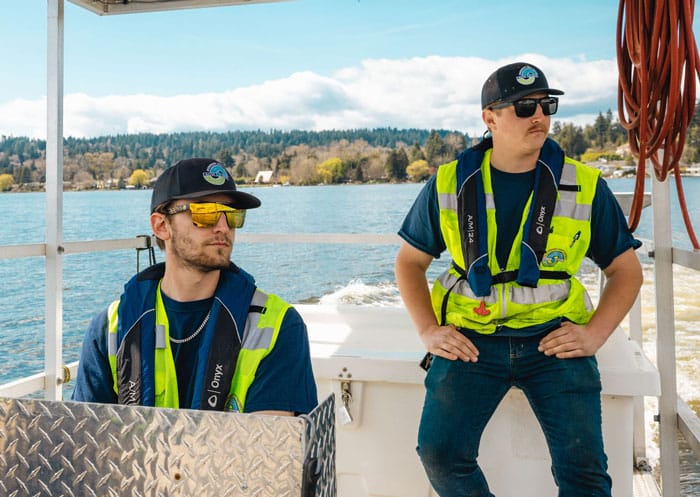 two workers in protective gear sitting on an industrial boat in the middle of the lake