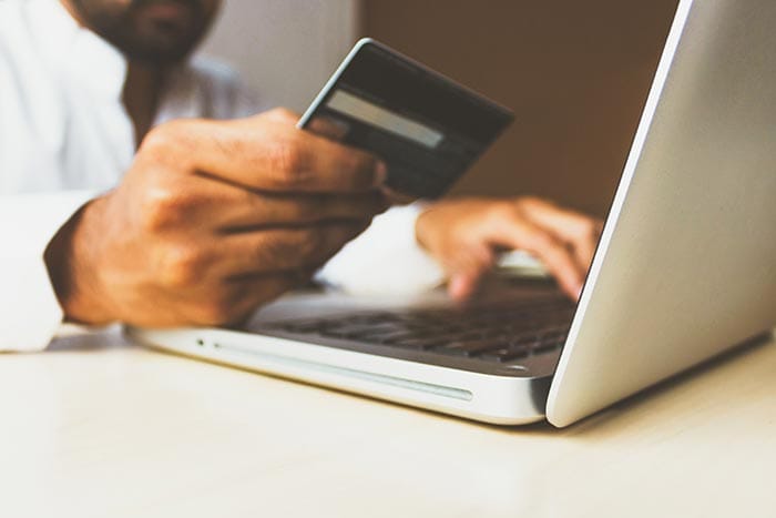 a man holding up a credit card and typing on a laptop