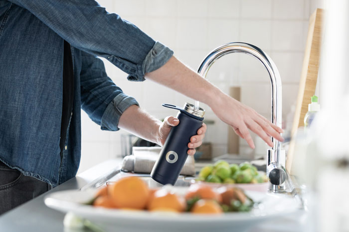 a person filling up a water bottle from their kitchen faucet