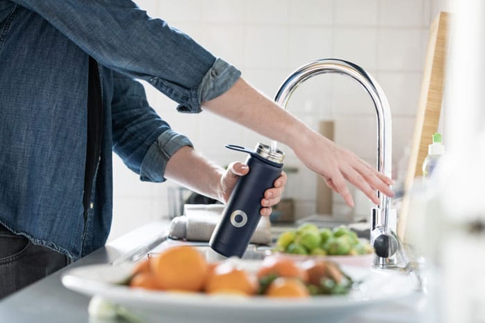 a person filling up a water bottle from their kitchen faucet