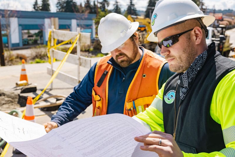 two workers in protective gear examining a large sheet of paper