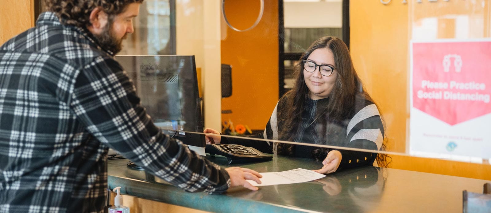 a smiling woman handing paperwork to a client across the counter